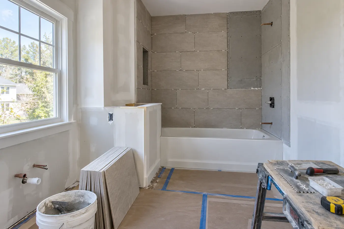Bathroom renovation in progress with staged tiles, protected flooring and tools